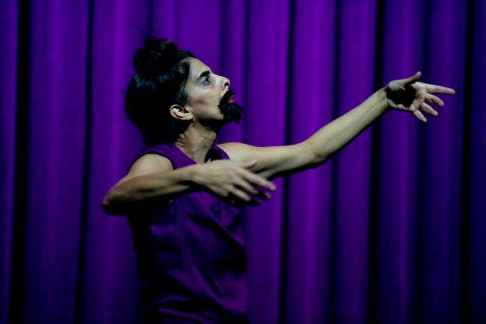 Une femme avec une barbe danse seule devant un rideau violet