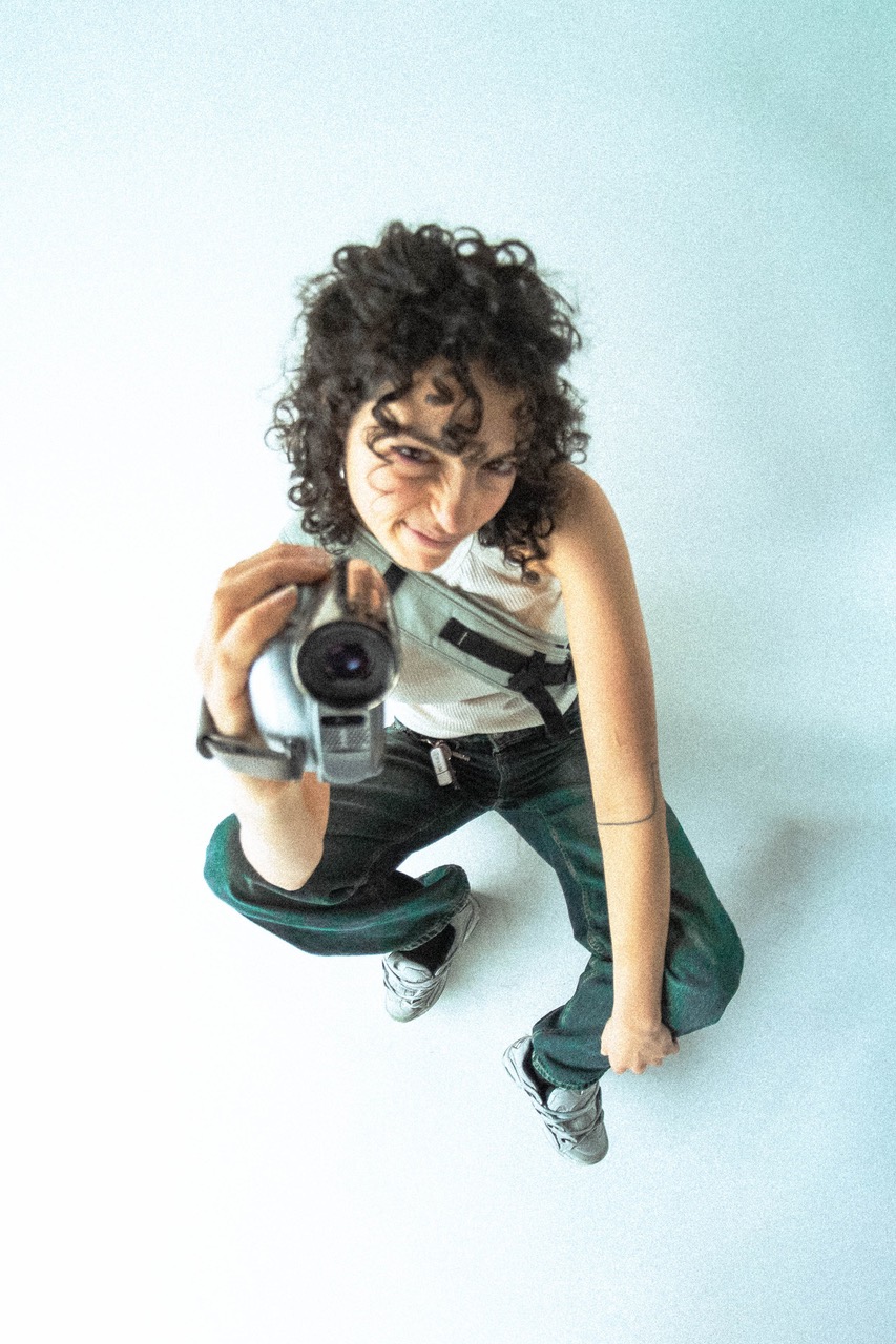 Une femme accroupie brandissant une caméra face à l'objectif du photographe.