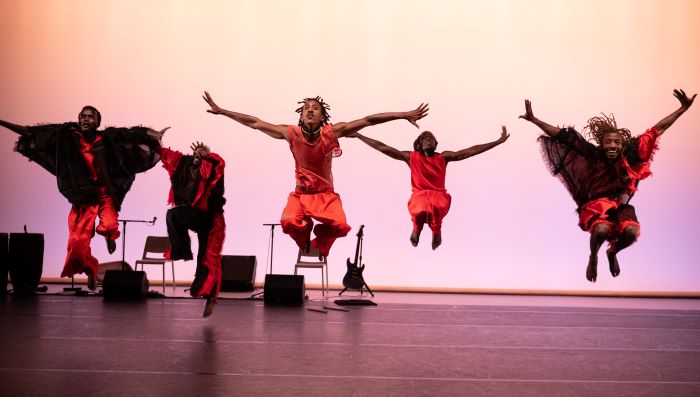 Cinq danseurs en orange en suspension. Photo prise alors qu'ils sont tous en train de sauter.