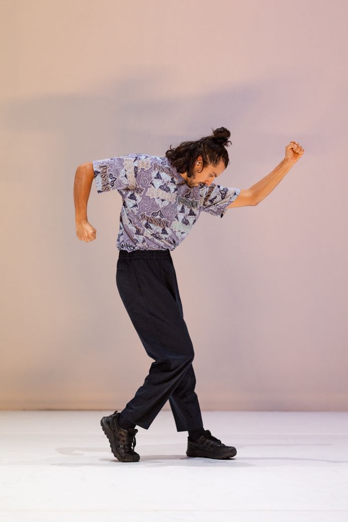 Danseur en mouvement de profil jambe droite plié et bras gauche levé et droit baissé, poings serrés.